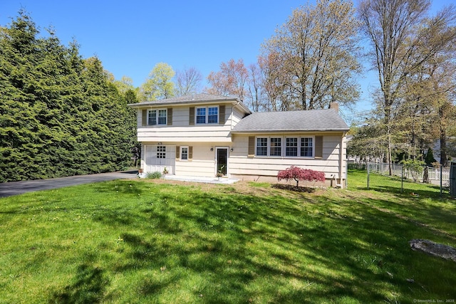 split level home with aphalt driveway, fence, a front yard, and a chimney