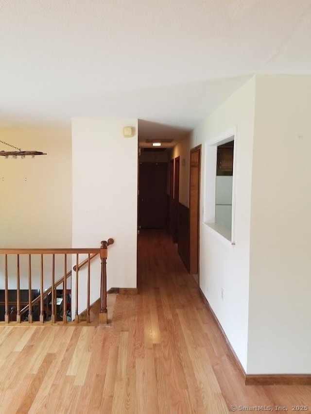 corridor featuring baseboards, an upstairs landing, and light wood-style flooring