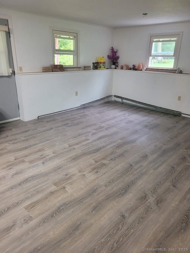unfurnished room featuring plenty of natural light, a baseboard radiator, and wood finished floors