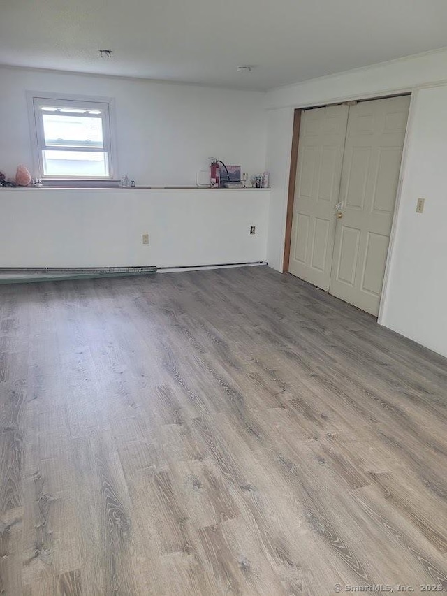 unfurnished bedroom featuring a closet, a baseboard heating unit, and wood finished floors