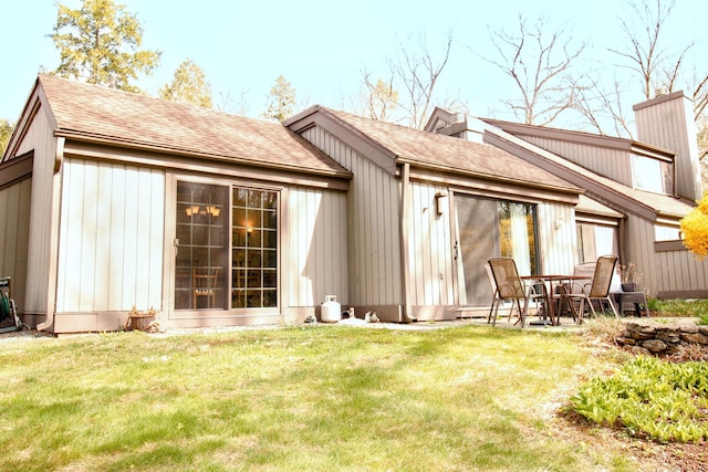 back of property featuring roof with shingles, a chimney, and a yard