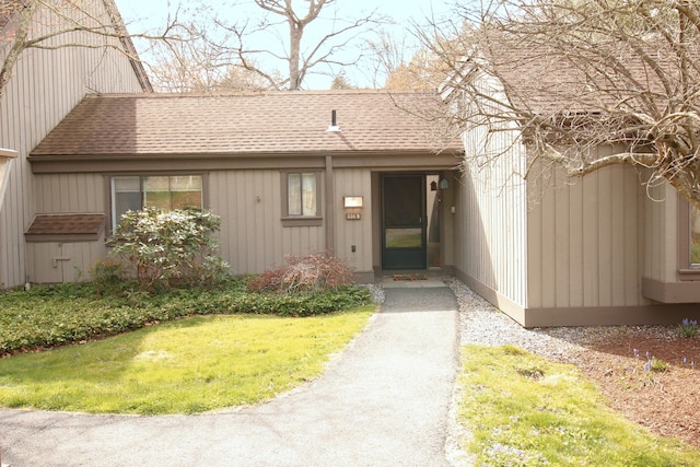 view of exterior entry with a shingled roof and a yard