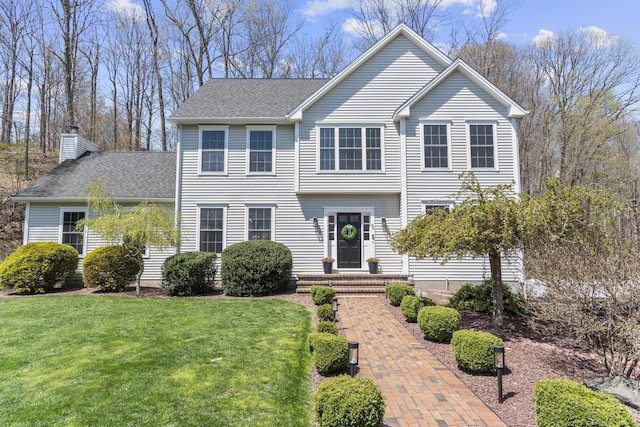 view of front of house featuring a chimney, a front yard, and a shingled roof
