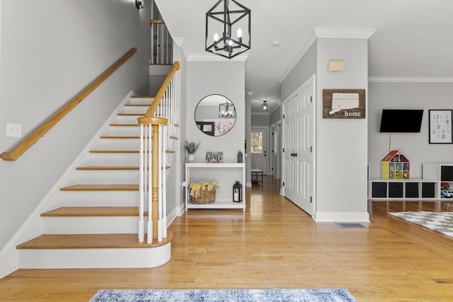 stairway featuring crown molding, visible vents, baseboards, an inviting chandelier, and wood finished floors