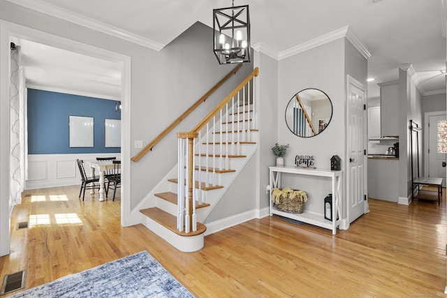 stairs featuring visible vents, wood finished floors, a notable chandelier, and crown molding