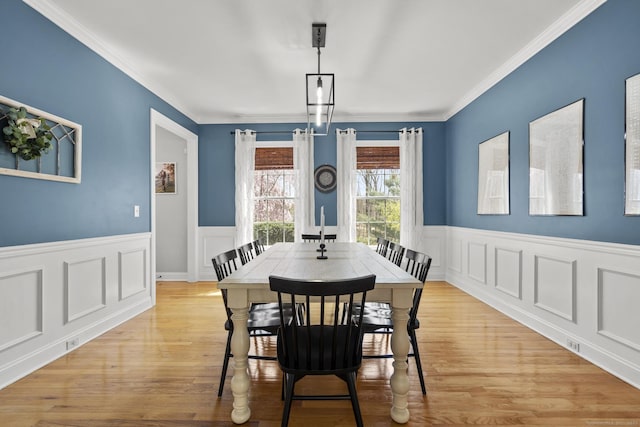 dining room featuring ornamental molding, a wainscoted wall, light wood-style flooring, and a decorative wall