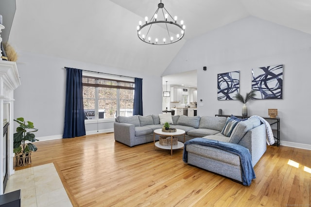 living room with an inviting chandelier, light wood-style floors, high vaulted ceiling, and baseboards