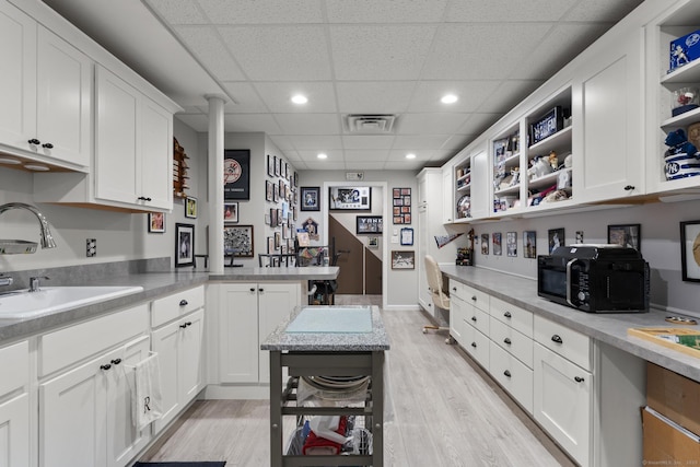 kitchen with open shelves, light wood-style floors, white cabinets, a sink, and a paneled ceiling