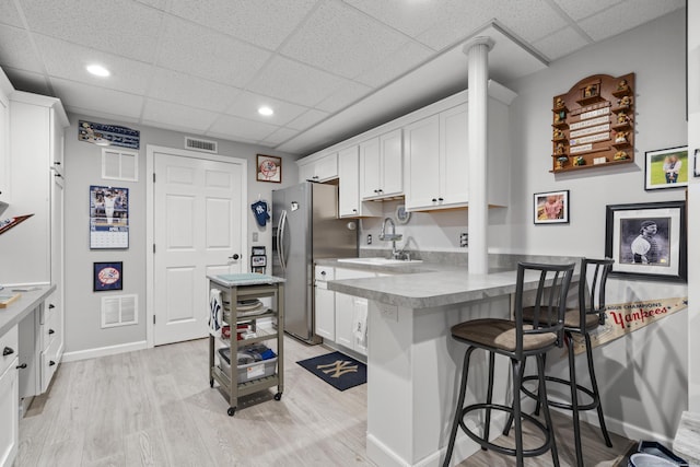 kitchen featuring a sink, visible vents, freestanding refrigerator, white cabinets, and a drop ceiling