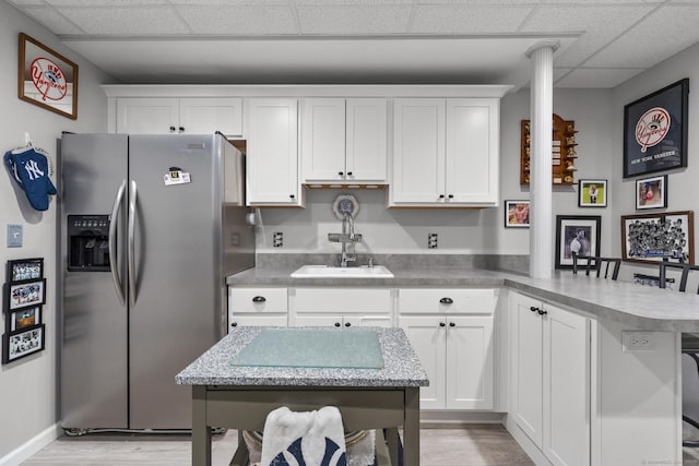 kitchen featuring a sink, stainless steel refrigerator with ice dispenser, a peninsula, white cabinets, and a drop ceiling