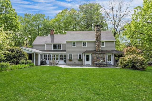 rear view of house featuring a chimney, a patio, a lawn, and stone siding