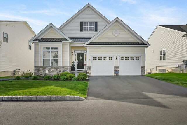 craftsman-style home featuring a garage, a front lawn, stone siding, a standing seam roof, and driveway