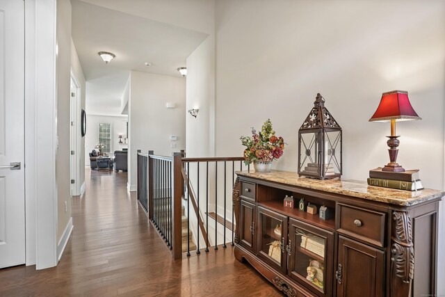hall featuring dark wood-style flooring, baseboards, and an upstairs landing