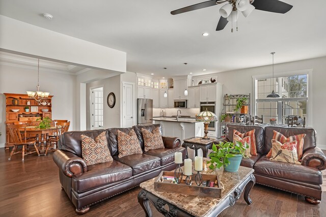 living room with recessed lighting, ornamental molding, ceiling fan with notable chandelier, and dark wood finished floors