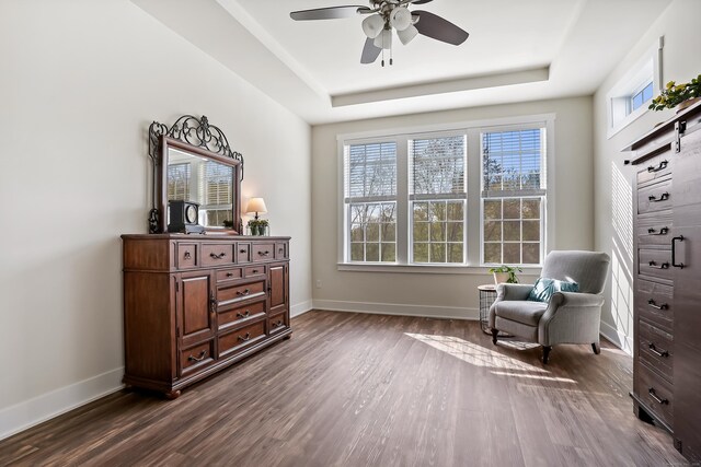 living area featuring a ceiling fan, baseboards, dark wood-style floors, and a tray ceiling