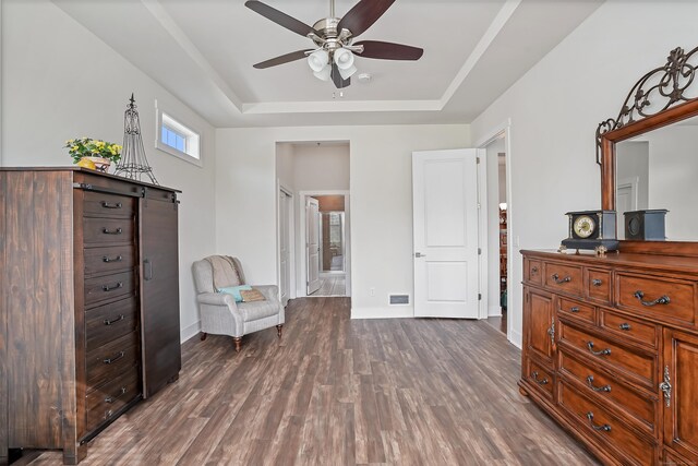 sitting room with ceiling fan, a tray ceiling, dark wood finished floors, and visible vents
