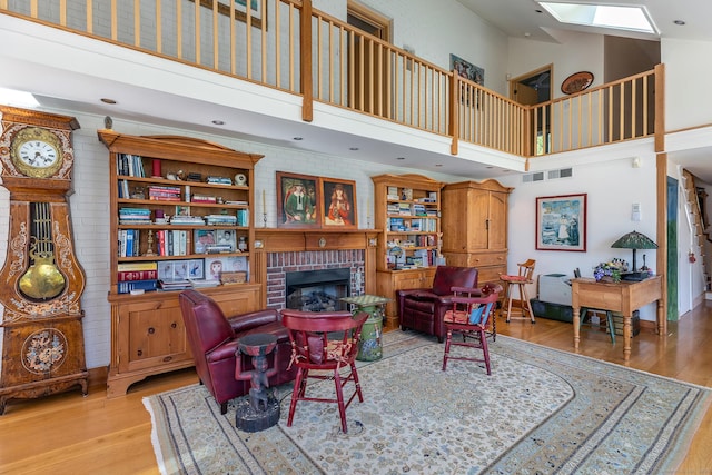 living area featuring visible vents, a brick fireplace, wood finished floors, high vaulted ceiling, and a skylight