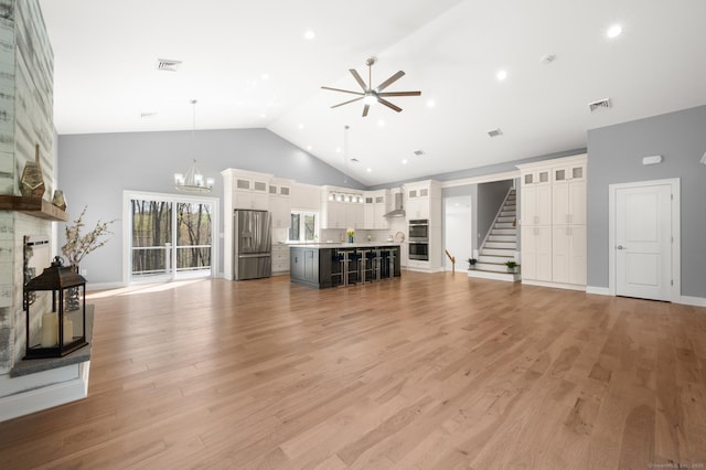 unfurnished living room featuring high vaulted ceiling, ceiling fan with notable chandelier, stairs, and visible vents
