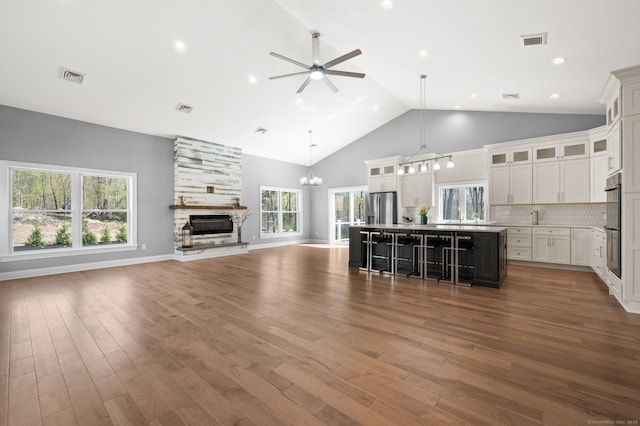 unfurnished living room with visible vents, wood finished floors, ceiling fan with notable chandelier, and a fireplace