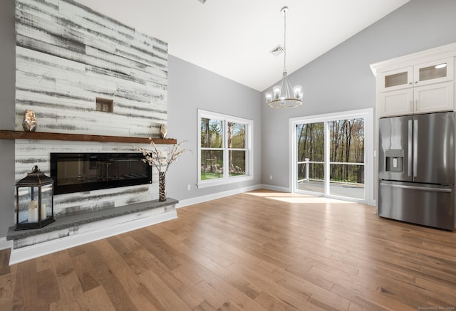 unfurnished living room featuring a glass covered fireplace, wood finished floors, baseboards, high vaulted ceiling, and a notable chandelier