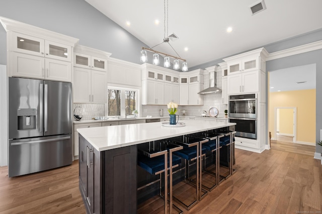 kitchen with wall chimney range hood, visible vents, light countertops, stainless steel appliances, and a spacious island