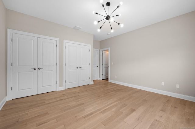 unfurnished bedroom featuring visible vents, multiple closets, baseboards, light wood-type flooring, and a chandelier