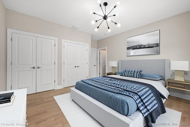 bedroom with two closets, light wood-style flooring, and a chandelier