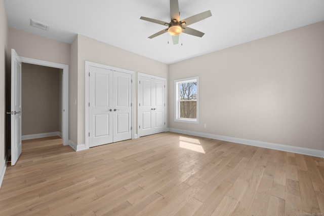 unfurnished bedroom with visible vents, multiple closets, light wood finished floors, and baseboards