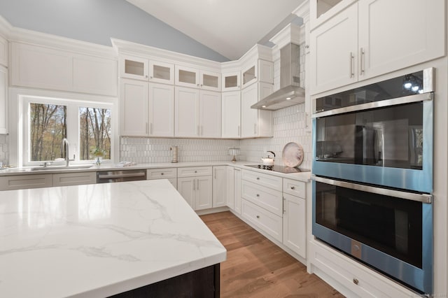 kitchen featuring tasteful backsplash, vaulted ceiling, a sink, light wood-style floors, and stainless steel appliances