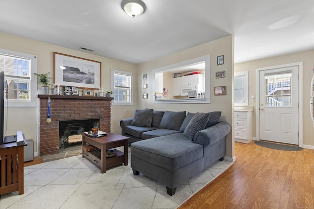 living room featuring a fireplace, baseboards, visible vents, and light wood-style floors