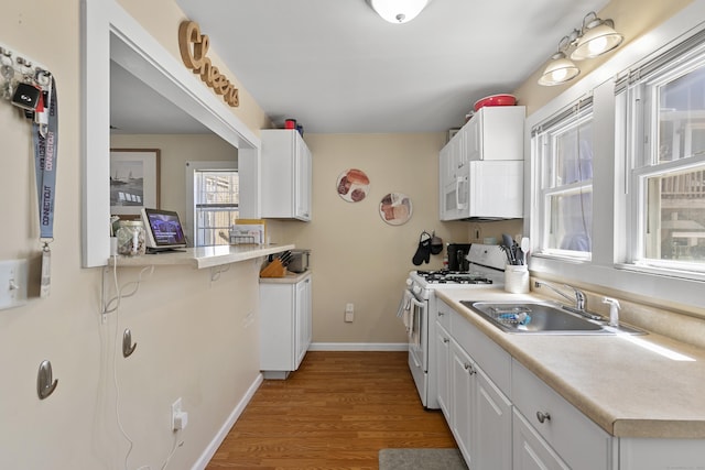 kitchen featuring white appliances, light wood-style floors, light countertops, white cabinets, and a sink