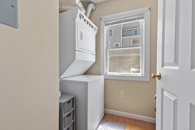 laundry area with light wood-style floors, baseboards, laundry area, and stacked washer / dryer