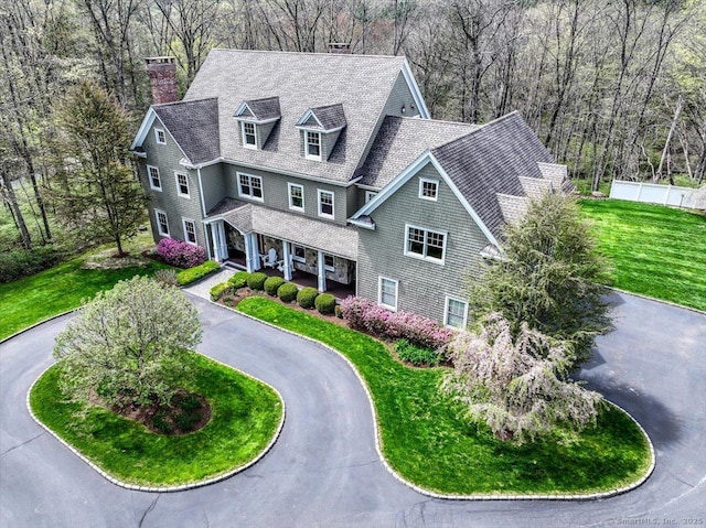 view of front of home with a chimney, a shingled roof, covered porch, curved driveway, and fence