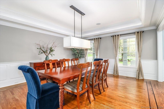 dining area featuring a raised ceiling, a wainscoted wall, ornamental molding, and light wood-style flooring