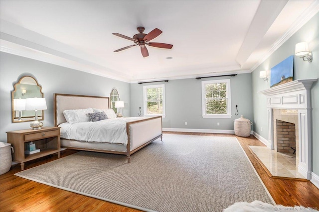 bedroom featuring baseboards, wood finished floors, a premium fireplace, and crown molding