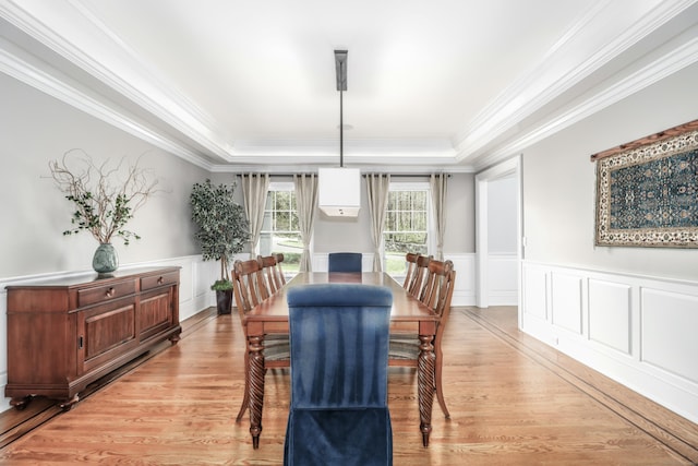 dining space featuring light wood-style floors, a raised ceiling, a decorative wall, ornamental molding, and wainscoting