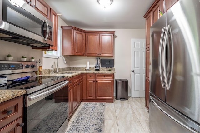 kitchen with brown cabinets, a sink, light stone counters, and stainless steel appliances