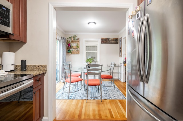 kitchen featuring light stone countertops, wood finished floors, brown cabinetry, appliances with stainless steel finishes, and ornamental molding