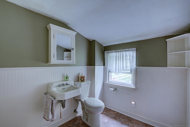 bathroom with vaulted ceiling, toilet, a sink, and wainscoting