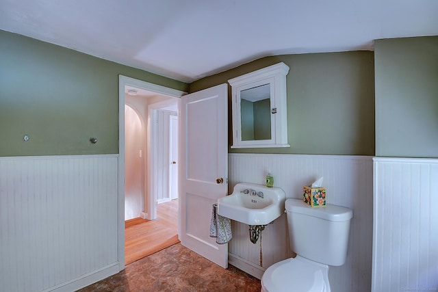 bathroom with a wainscoted wall, toilet, a sink, and wood walls