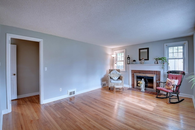living area featuring a brick fireplace, wood finished floors, plenty of natural light, a textured ceiling, and baseboards