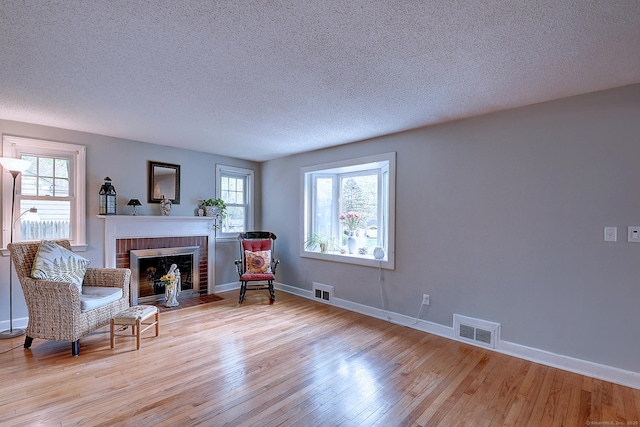 sitting room featuring wood finished floors, a brick fireplace, a textured ceiling, plenty of natural light, and baseboards