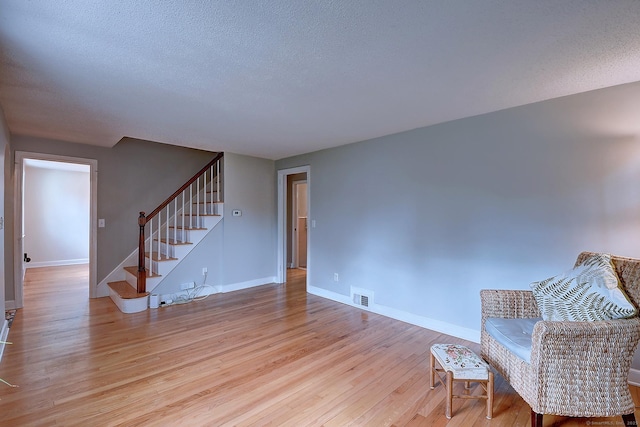 sitting room with stairs, light wood finished floors, baseboards, and a textured ceiling