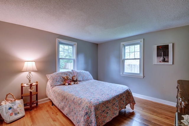 bedroom with baseboards, light wood-style floors, and a textured ceiling