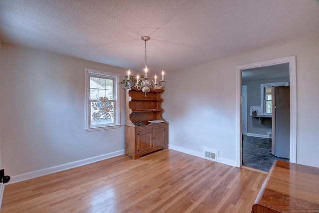 unfurnished dining area featuring a chandelier, light wood-style flooring, a textured ceiling, and baseboards