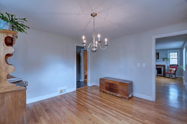 unfurnished dining area with wood finished floors, a chandelier, a brick fireplace, baseboards, and a textured ceiling