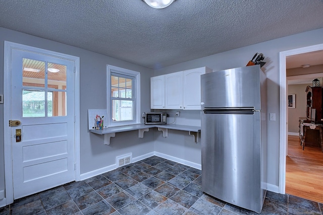 kitchen with freestanding refrigerator, white cabinets, baseboards, light countertops, and a textured ceiling