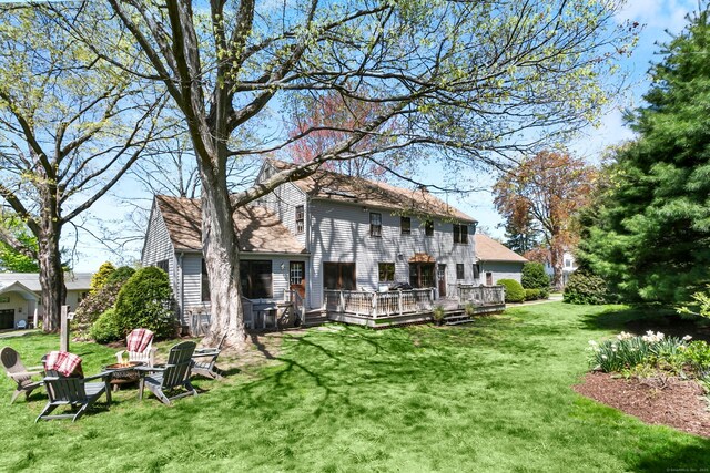 rear view of property with a yard, a wooden deck, and an outdoor fire pit