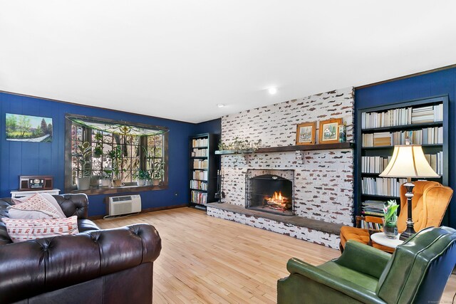 living area with a wall unit AC, a tile fireplace, wood finished floors, baseboards, and an accent wall