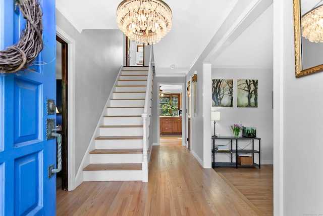 entryway with wood finished floors, stairway, baseboards, a notable chandelier, and ornamental molding